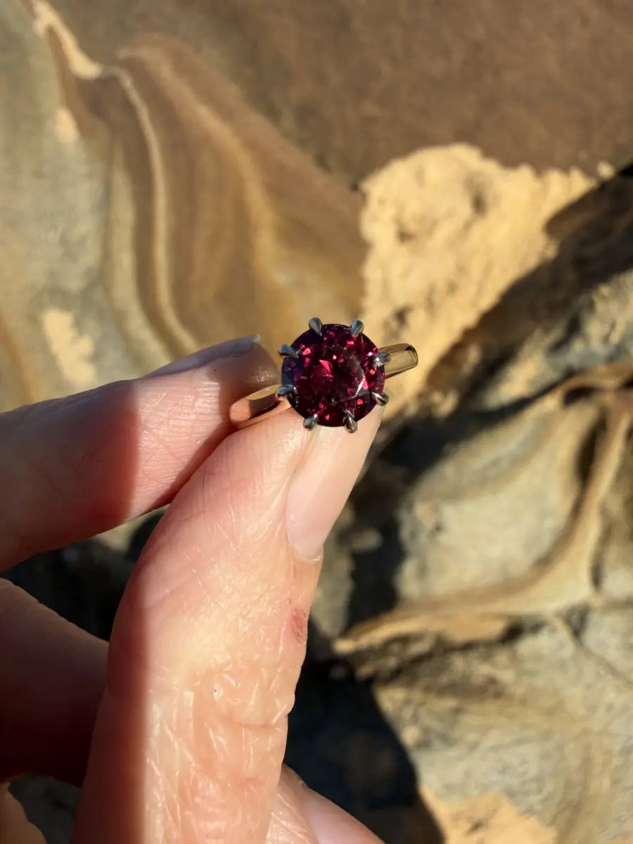 A bespoke ring with a deep red round stone, held up against sandstone