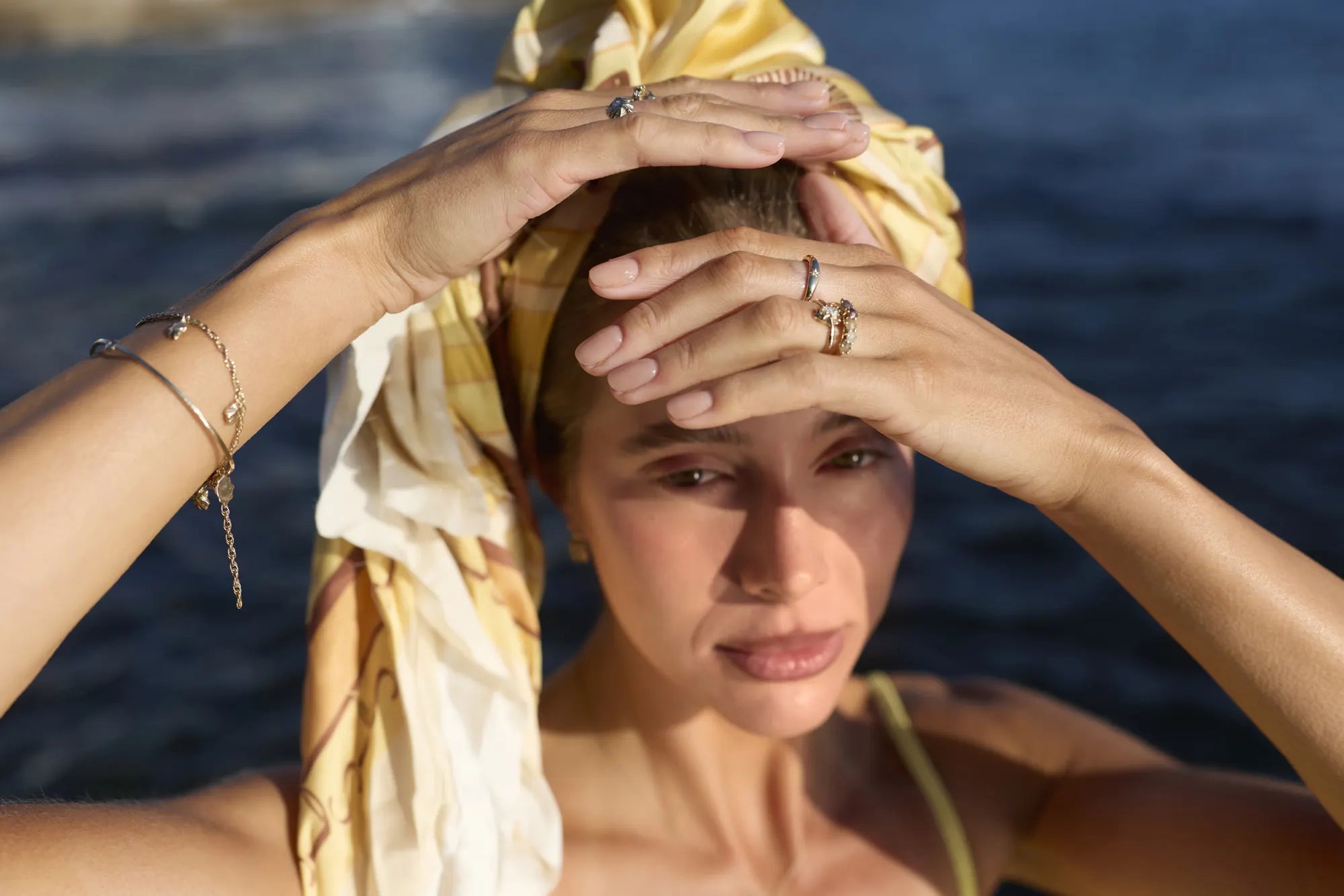 A woman shades her eyes in the sun by the sea, wearing Star Limpet rings and bracelets