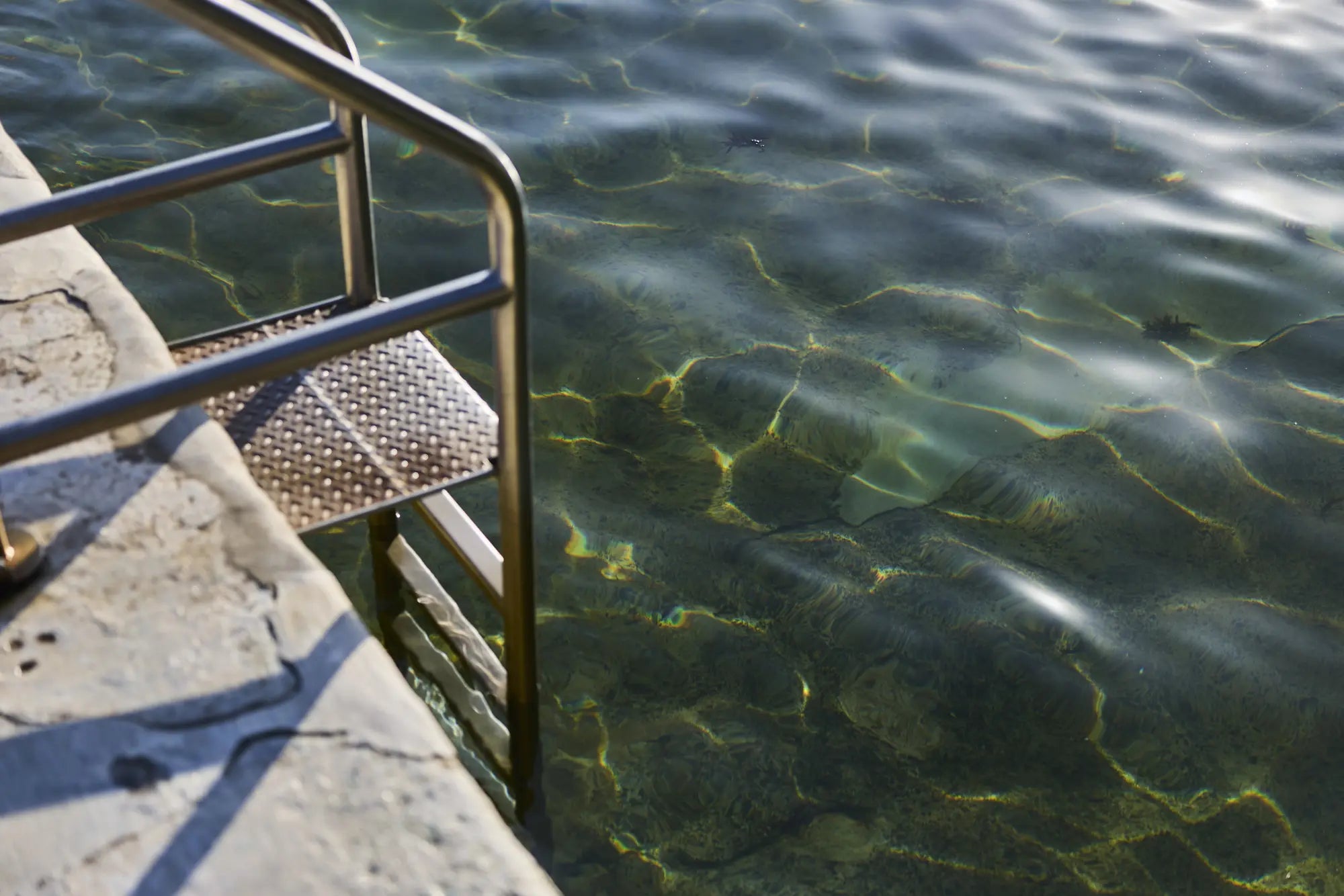 Sunlight patterns in green water beside a rock pool ladder