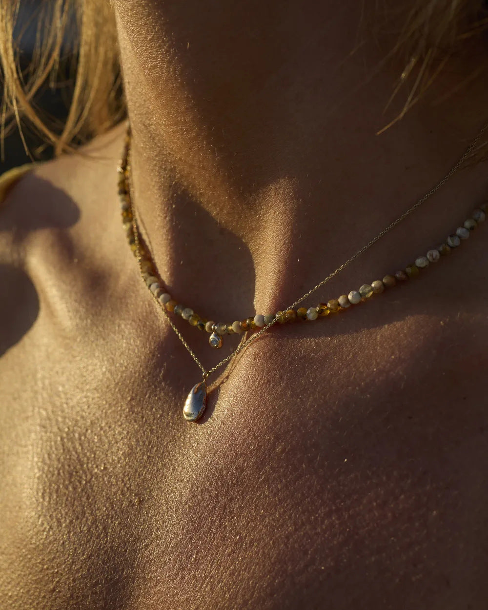 Gold mussel shell pendant worn at the collarbone in golden light