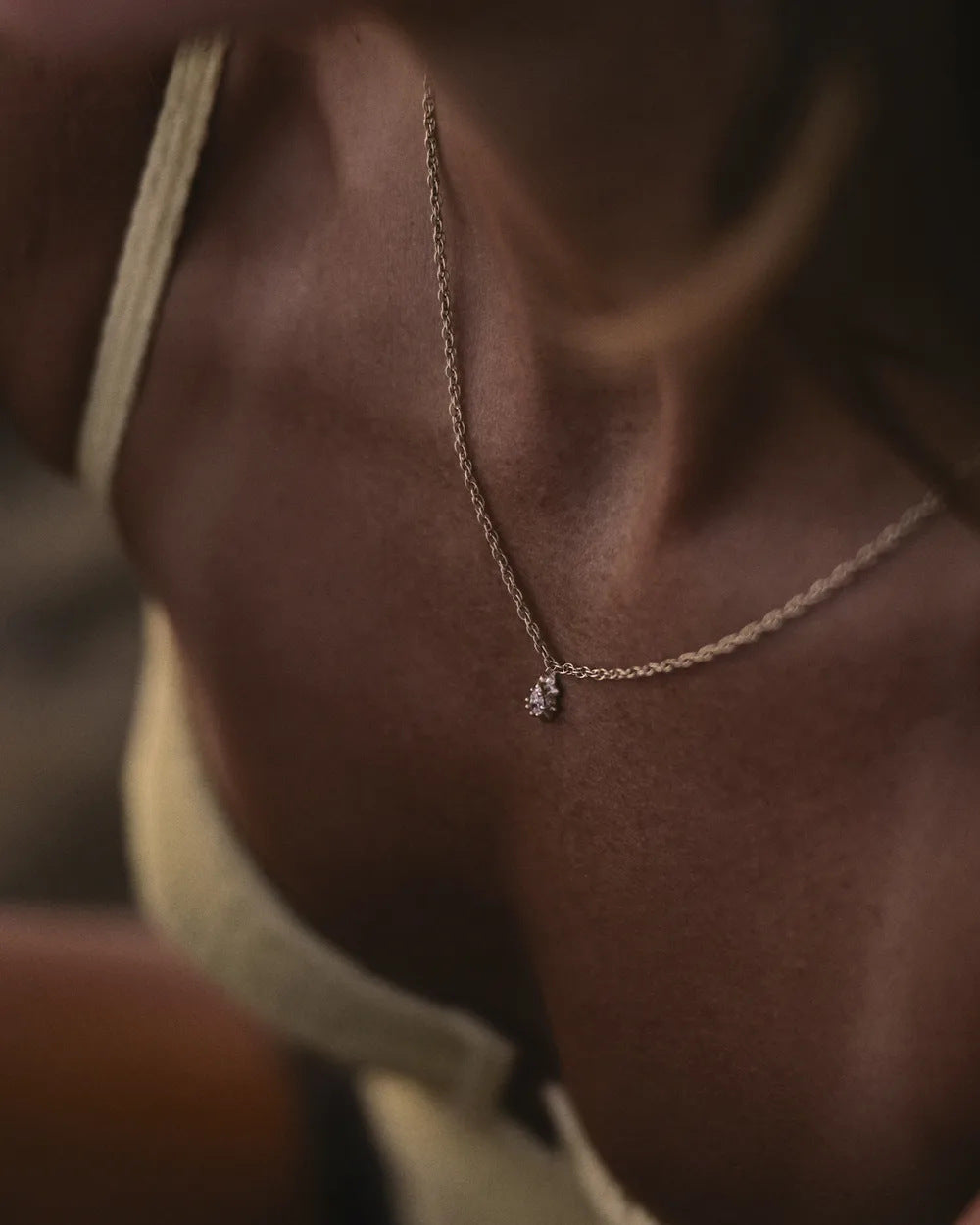 Pear diamond pendant worn at the collarbone in golden light