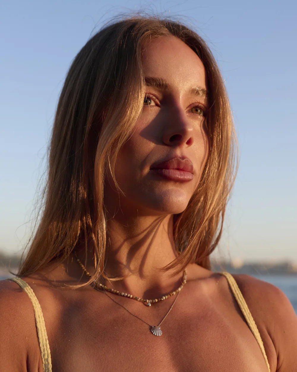 Gold scallop shell pendant worn with a beaded necklace by the sea