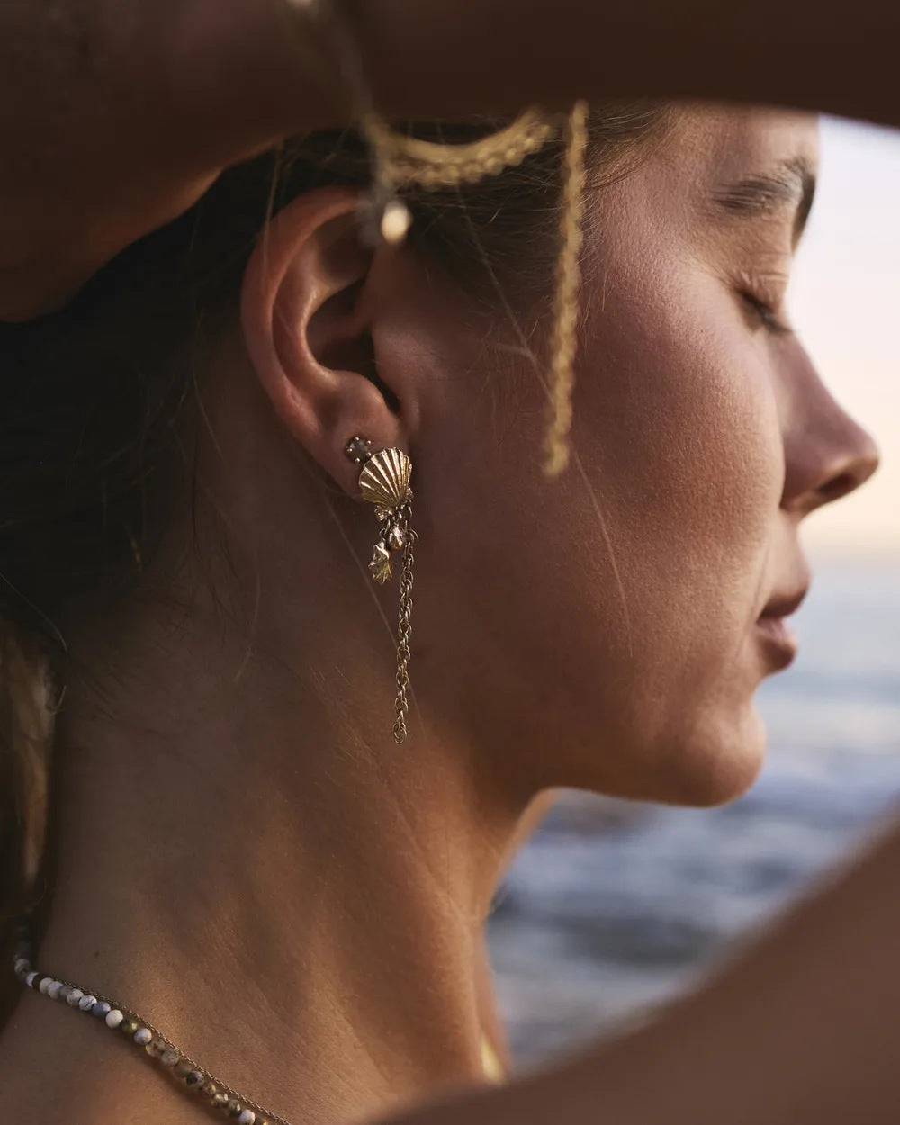 Statement shell earring worn at the ear by the sea at sunset